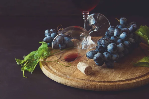 İki kadehlerin kırmızı şarap ve üzüm asma yaprağı koyu ahşap masa üzerine dekore edilmiştir.