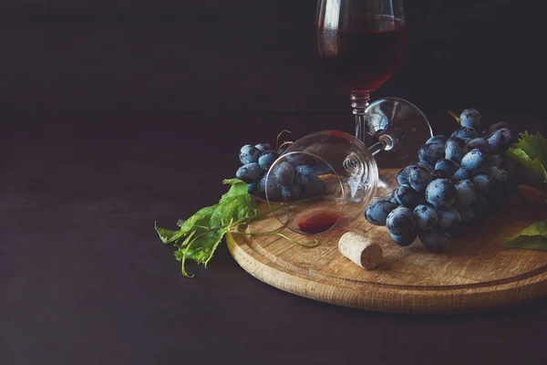 Dos copas de vino con vino tinto y hojas de vid decoradas con uvas sobre un escritorio de madera oscura — Foto de Stock