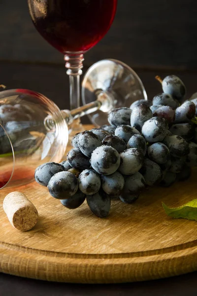 Dos copas de vino con vino tinto y hojas de vid decoradas con uvas sobre un escritorio de madera oscura — Foto de Stock