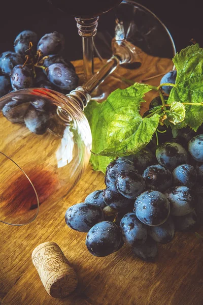 Dva pohárky s červeným vínem a hrozny zdobené vinné listy na tmavý dřevěný stůl — Stock fotografie