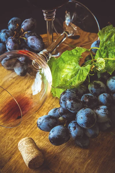 Two wineglasses with red wine and grapes decorated vine leaves on dark wooden desk — Stock Photo, Image