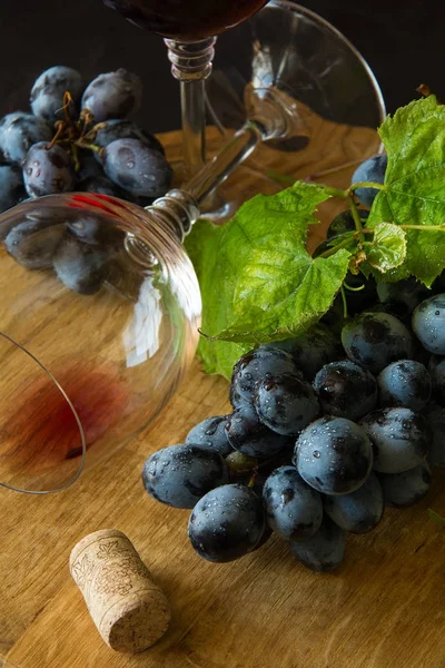 İki kadehlerin kırmızı şarap ve üzüm asma yaprağı koyu ahşap masa üzerine dekore edilmiştir.