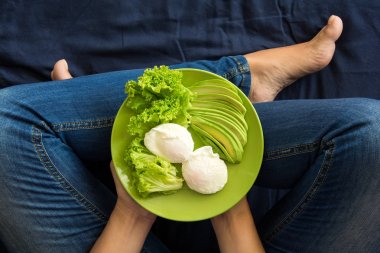 Sağlıklı beslenme kavramı. Kadınların elleri marul, avokado dilimleri ve haşlanmış yumurta ile plaka tutarak. Üstten Görünüm
