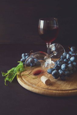 İki kadehlerin kırmızı şarap ve üzüm asma yaprağı koyu ahşap masa üzerine dekore edilmiştir.