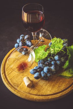 İki kadehlerin kırmızı şarap ve üzüm asma yaprağı koyu ahşap masa üzerine dekore edilmiştir.