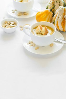 İki bardak taze kabak kremalı çorba ile dekore edilmiş krem, tohum ve kraker üzerinde beyaz masa örtüsü