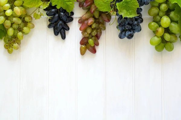 Uvas coloridas deitadas sobre fundo branco de madeira — Fotografia de Stock