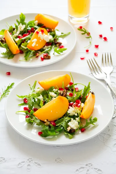 Fresh autumn salad with persimmon, arugula, cheese and pomegranate seeds on white table cloth. Space for copy — Stock Photo, Image