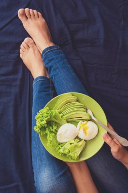 Sağlıklı beslenme kavramı. Kadınların elleri marul, avokado dilimleri ve haşlanmış yumurta ile plaka tutarak. Üstten Görünüm