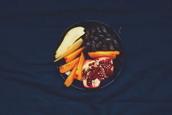 Concepto de alimentación saludable. Manos de mujer sosteniendo plato con peras, uvas, caqui y frutos de granada. Vista superior — Foto de Stock