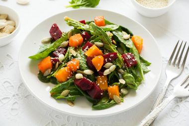 Marine kabak ve pancar taze sonbahar salatası, ıspanak yaprakları, zeytinyağı, susam ve beyaz masa örtüsü üzerinde kabak çekirdeği. Kopya için alan