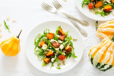 Fırında kabak, roka, peynir ve tohumlar beyaz masa örtüsü üzerinde taze sonbahar salatası. Kopya için alan