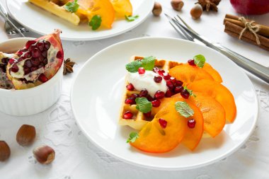 Trabzon hurması, nar taneleri ve beyaz masa örtüsü üzerinde ekşi krema ile Belçika waffle plakaları