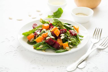 Marine kabak ve pancar taze sonbahar salatası, ıspanak yaprakları, zeytinyağı, susam ve beyaz masa örtüsü üzerinde kabak çekirdeği. Kopya için alan