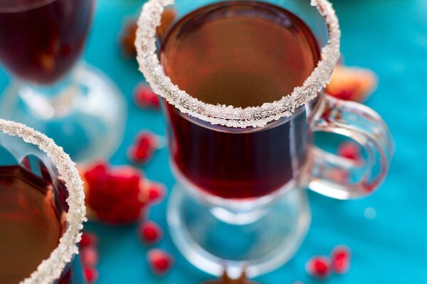 Three glasses of hot mulled wine with pomegranate seeds and spices on turquoise background