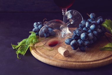 İki kadehlerin kırmızı şarap ve üzüm asma yaprağı koyu ahşap masa üzerine dekore edilmiştir.