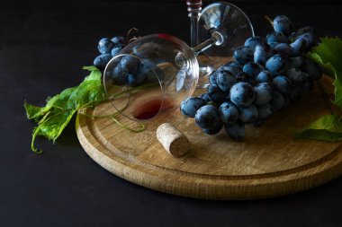 İki kadehlerin kırmızı şarap ve üzüm asma yaprağı koyu ahşap masa üzerine dekore edilmiştir.