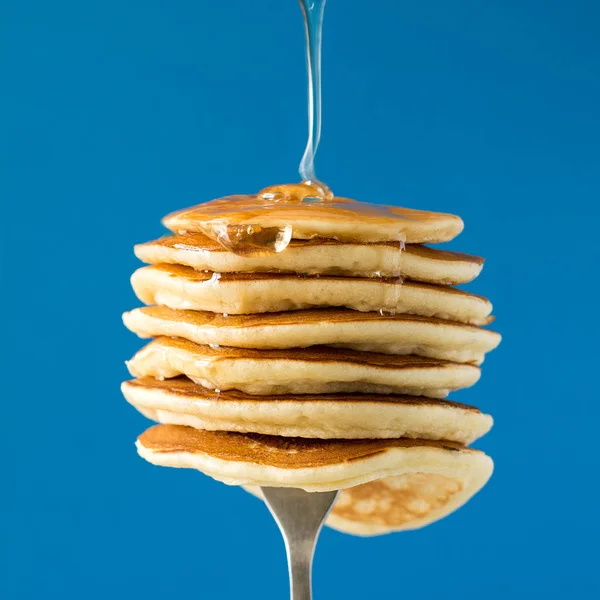 在蓝色背景的叉子上用蜂蜜装饰的甜樱桃叠的薄饼 — 图库照片
