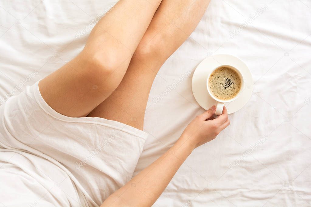 Soft photo of woman on the bed with cup of coffee. Top view