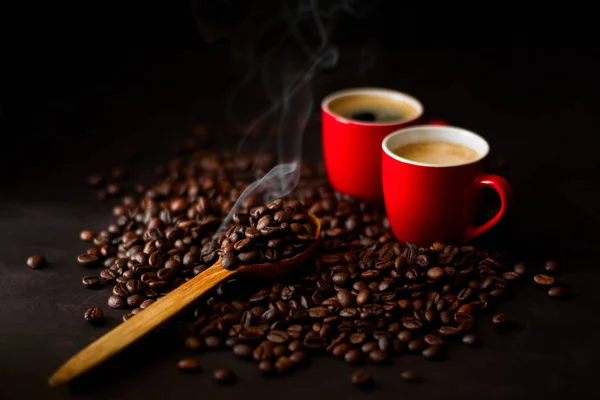 Twee rode kopjes espresso met koffiebonen op donkere houten backgr — Stockfoto