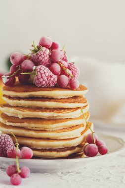Ahududu, kırmızı kuş üzümü, krem ile krep yığını ve beyaz masa örtüsü üzerinde bal