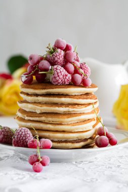 Ahududu, kırmızı kuş üzümü, krem ile krep yığını ve beyaz masa örtüsü üzerinde bal