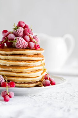 Ahududu, kırmızı kuş üzümü, krem ile krep yığını ve beyaz masa örtüsü üzerinde bal