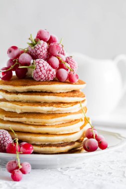 Ahududu, kırmızı kuş üzümü, krem ile krep yığını ve beyaz masa örtüsü üzerinde bal