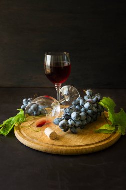 İki kadehlerin kırmızı şarap ve üzüm asma yaprağı koyu ahşap masa üzerine dekore edilmiştir.