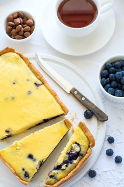 Çay saati. Ev yapımı yaban mersinli cheesecake, bardak çay, fındık ve berry beyaz masa örtüsü