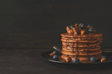 Krema, yaban mersini, badem, fındık ve çikolata parçaları ile çikolatalı krep yığını. Seçici odak. Tonda