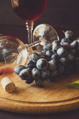 İki kadehlerin kırmızı şarap ve üzüm asma yaprağı koyu ahşap masa üzerine dekore edilmiştir. Tonda