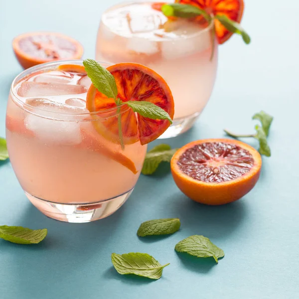 Blood orange cocktail with slices of orange on turquoise background