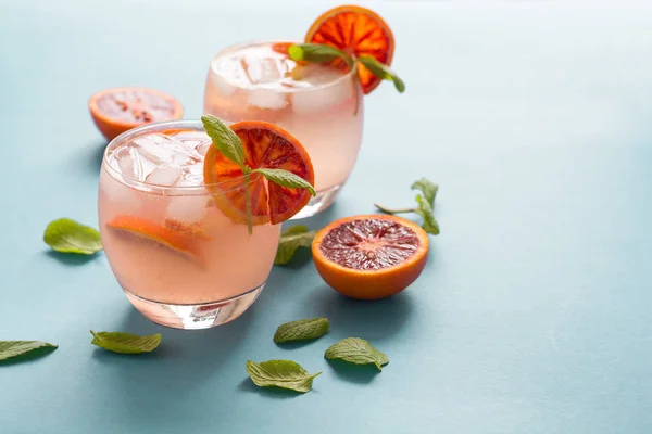 Blood orange cocktail with slices of orange on turquoise background