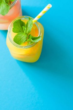 Portakal ve greyfurt limonata, dekore edilmiş buz ve mavi kağıt arka plan üzerine nane ile kavanoz.