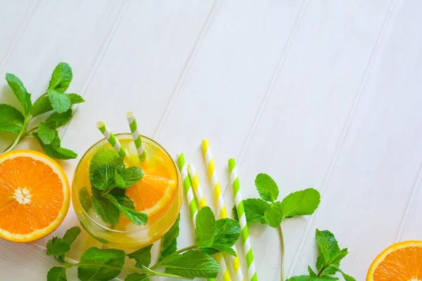 Orange lemonade with slices of orange, ice and mint on white wooden background. Top view. Copy space