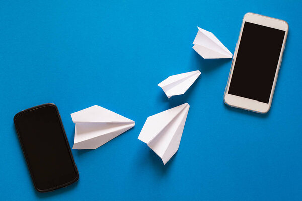 Data transfer concept. Message passing. Two mobile smartphones and paper airpaplanes on blue background. Origami. Paper cut.