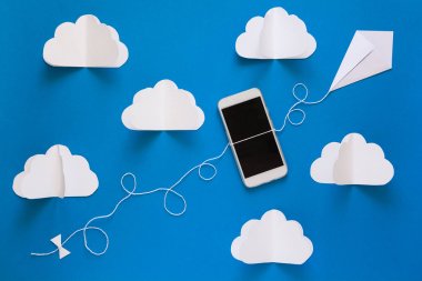 Ağ bağlantısı ve bulut depolama teknoloji kavramı. Veri iletişimi ve bulut bilgisayar ağ kavramı. Akıllı telefon üzerinde mavi gökyüzü kağıt uçurtma uçan. Origami. Kağıt kesiği. Üstten Görünüm