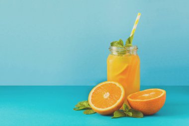 Kavanoz turuncu limonata ile dekore edilmiş buz ve nane mavi kağıt arka plan üzerinde. Tonda