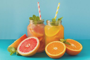 Portakal ve greyfurt limonata, dekore edilmiş buz ve mavi kağıt arka plan üzerine nane ile kavanoz. Tonda