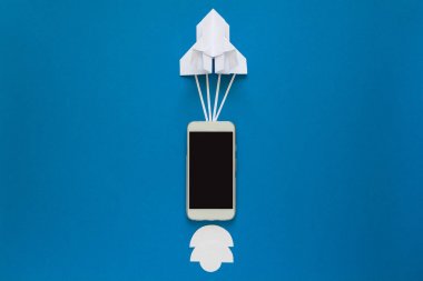 Başlamak yukarıya ya da bağlantı kavramı hızlı. Mavi gökyüzü bulutlar ile akıllı telefon ile denize indirmek kağıt roket. Origami. Kağıt kesiği. Üstten Görünüm