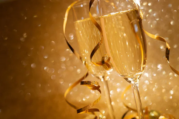 金色の輝く背景にシャンパンの装飾されたストリーマーの2つのメガネを閉じます クリスマスと新年の休暇の概念 スペースのコピー — ストック写真