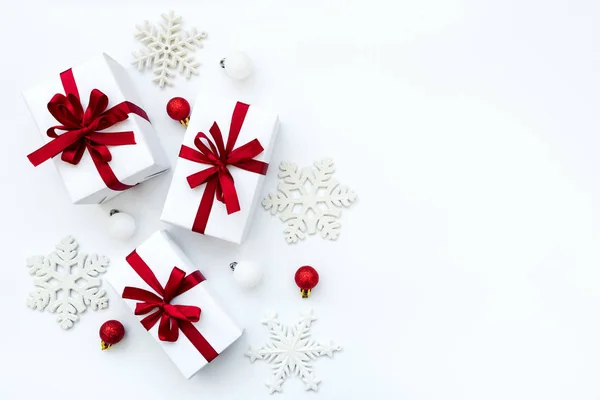 Hediye kutuları beyaz kağıda sarılı ve kırmızı kurdeleli mücevherler ve beyaz arka planda kar taneleri. Üst Manzara. Düz yatıyordu. Noel ve Yeni Yıl