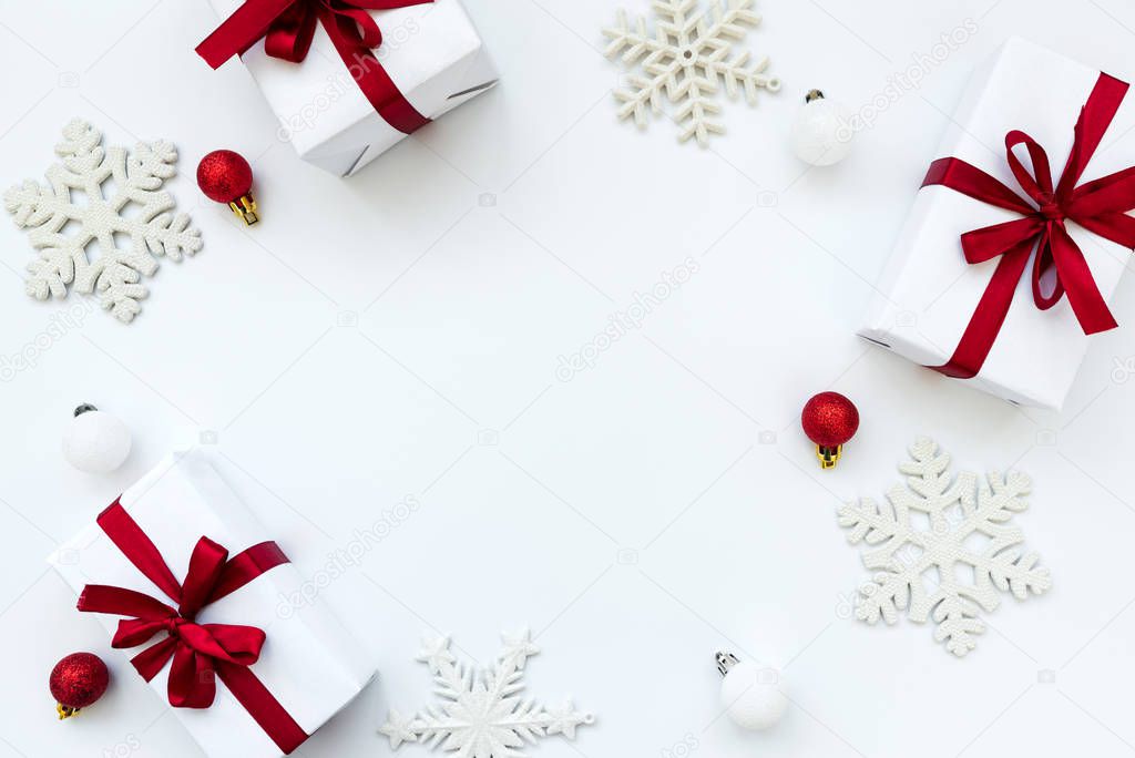 Frame from gift boxes wrapped white paper and red ribbon decorated baubles and snowflakes on white background. Top view. Flat lay.  Christmas and New year