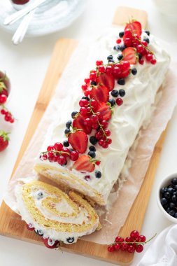 Krem şanti ve böğürtlen, yabanmersini ve kırmızı üzümlü beyaz ahşap arka planda kremalı kek rulosu. Yumuşak odaklanma. Yaz yemekleri konsepti