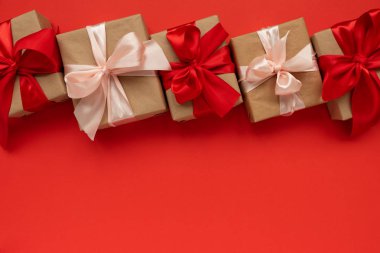 Hediye kutularının sınırı kahverengi el işi kağıtları ve kırmızı arka planda kırmızı ve pembe kurdeleler. Sevgililer Günü ya da Noel kutlaması konsepti. Üst görünüm