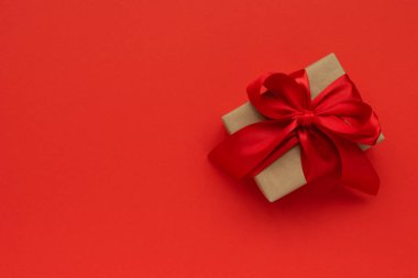 Hediye kutusu kahverengi el işi kağıt ve kırmızı arka planda kırmızı kurdele. Sevgililer Günü ya da Noel kutlaması konsepti. Üst görünüm