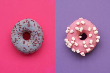 Mor arka planda pembe donut ve pembe arka planda mor donut süslemeleri. Düz yatıyordu. Üst Manzara. Sağlıksız yiyecekler