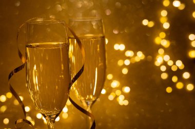 Odaklanamayan ışıklarla altın sarısı arka planda iki kadeh şampanya. Noel ve yeni yıl tatili konsepti. Uzayı kopyala Yumuşak odak