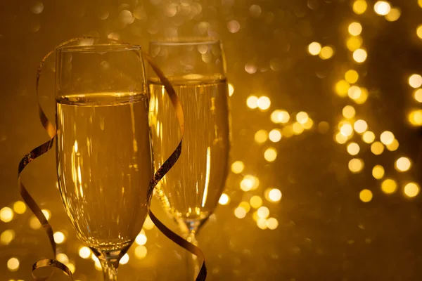 シャンパンの2つのガラスは 焦点を絞ったライトで金色の輝く背景にあります クリスマスと新年の休暇の概念 コピースペースソフトフォーカス — ストック写真